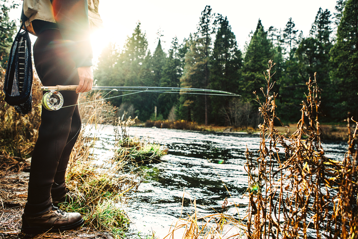 A fly fisherman views the Metolius river in central Oregon state, holding his rod and tackle. Emphasis and detail on the hand, pole and line. Horizontal with copy space.